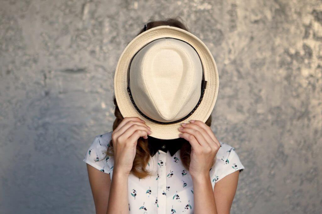 Chica oculta su cara con un sombrero porque siente un sentimiento de culpa